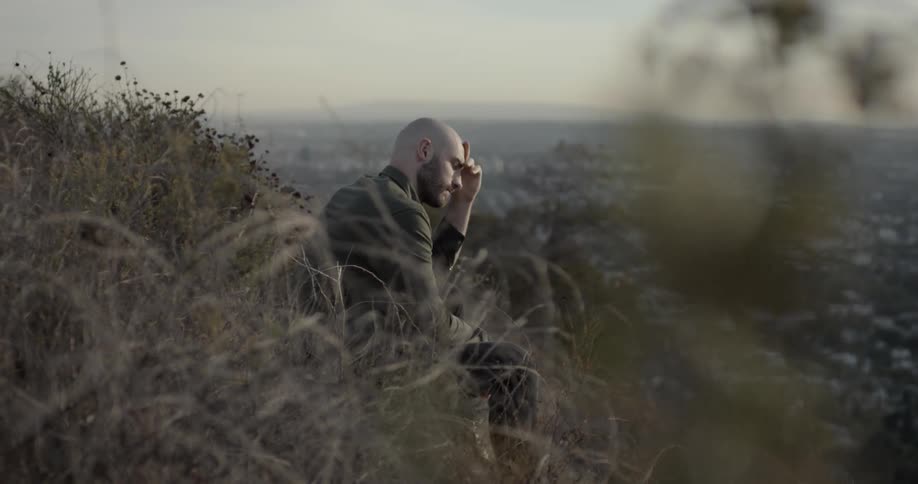 A man is looking at the skyline while sitting on a hill