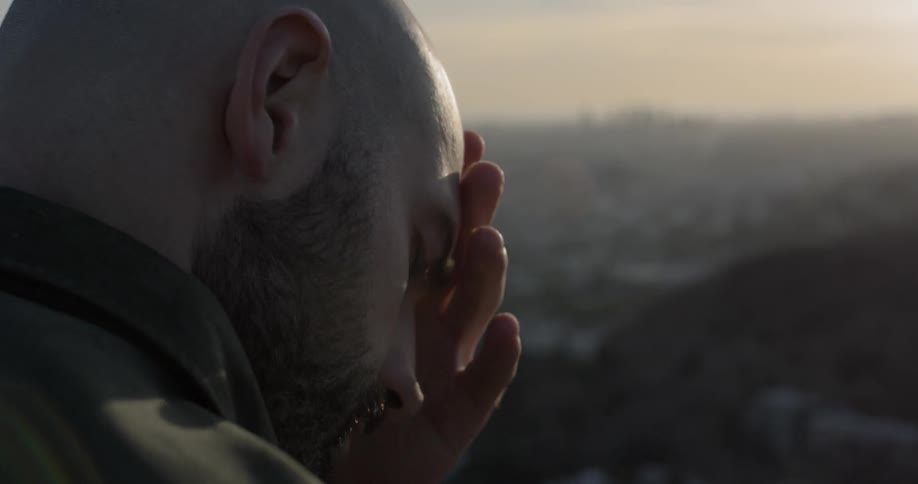Bald bearded man rubs his forehead with his hand and thinks outdoors