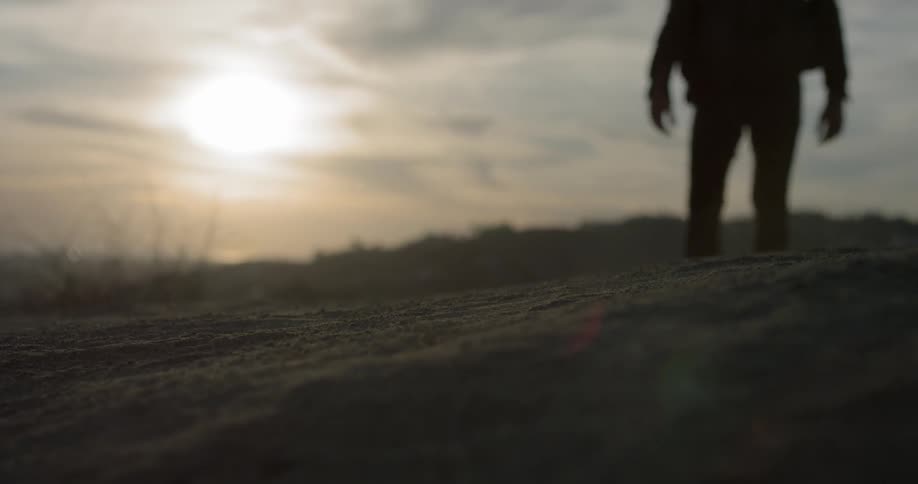Man walks along sand up slope under cloudy sky