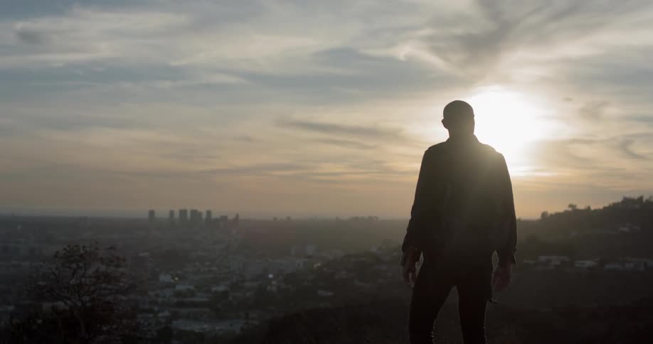 A man walking on a cliff with the city and the sky in the background