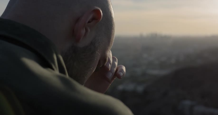 A man rubs his head and face while deep in thought at a picturesque overlook