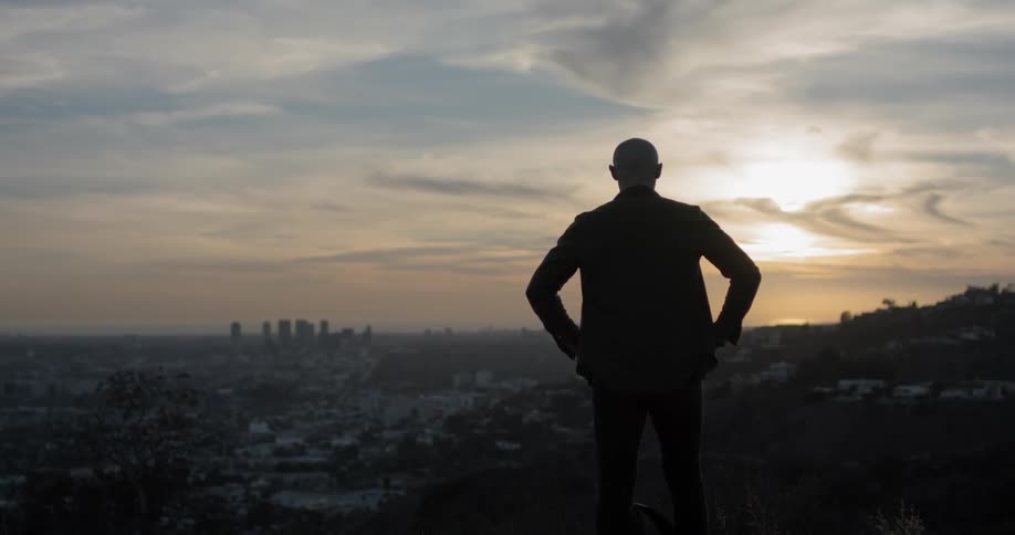 A white man stands on a hill and looks out over a large city