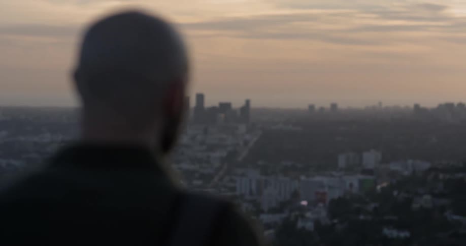 A man stands outside overlooking a city skyline at sunset