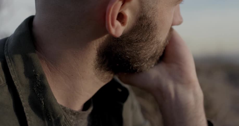 Bearded bald man sits and rubs his forehead during daylight