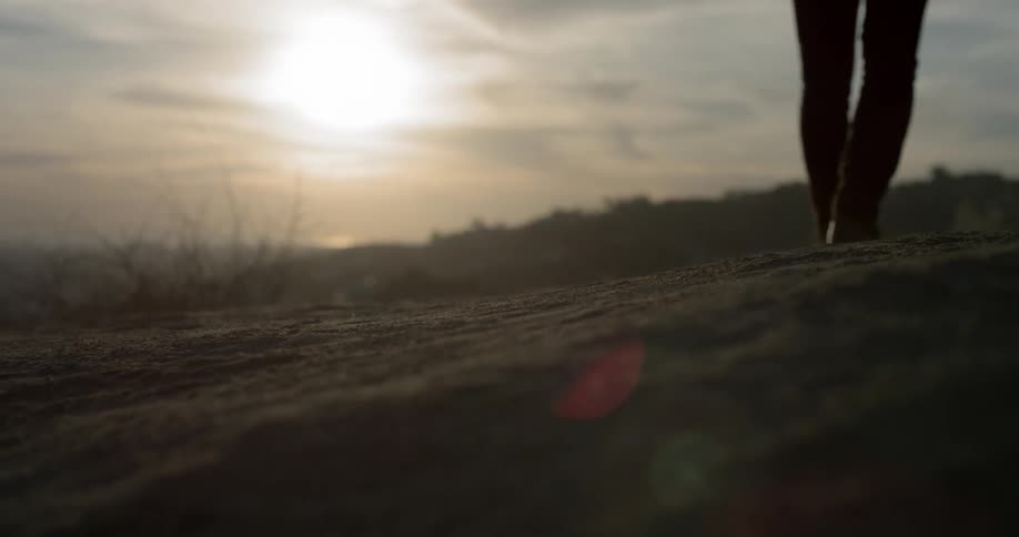 Man wearing boots walks the on the road raising dust as the sun sets