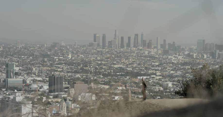A bald caucasian man climbing a hill overlooking a metropolis