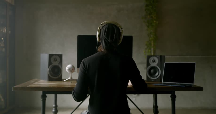 A man works on a computer using audio equipment and headphones