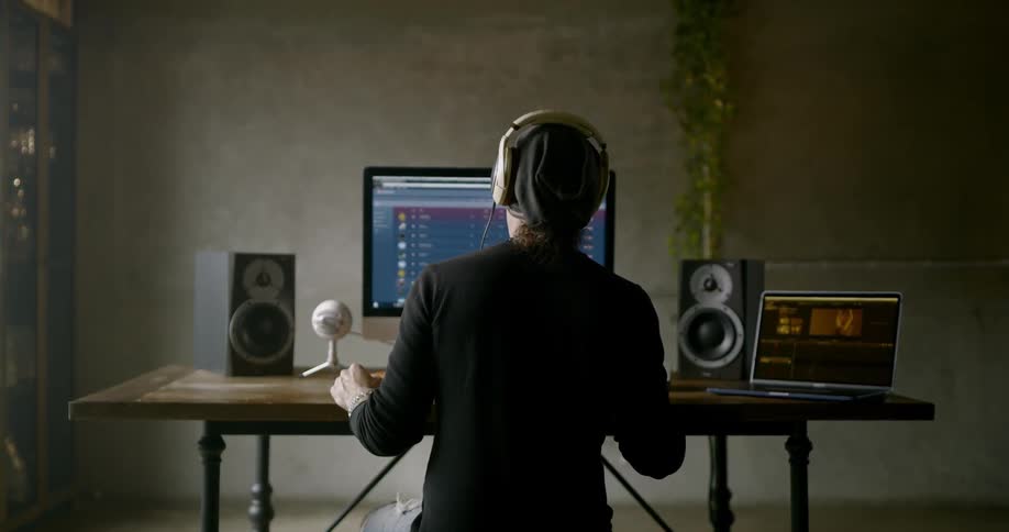 Man wearing headphones sits at the table and uses computer indoors during daylight
