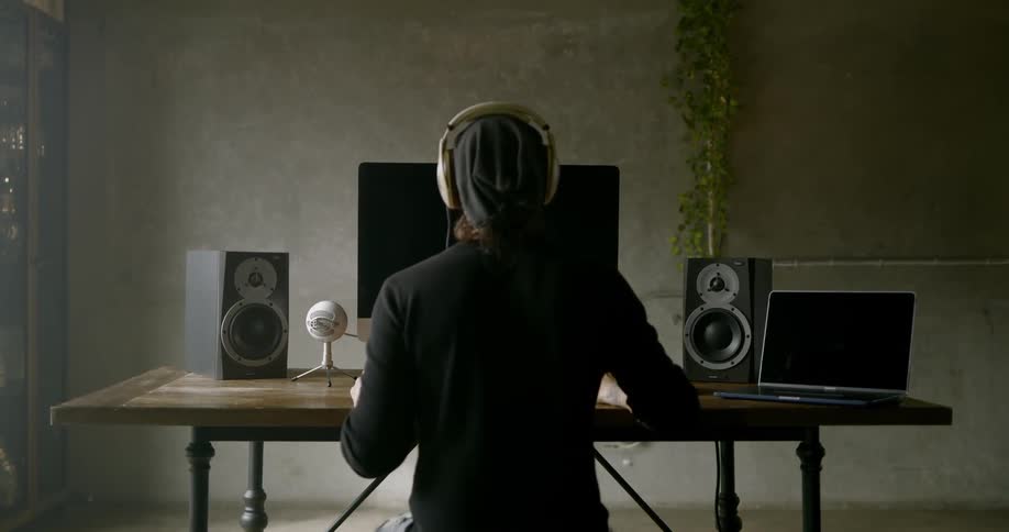 Man puts headphones on as he sits at a desk working on a computer