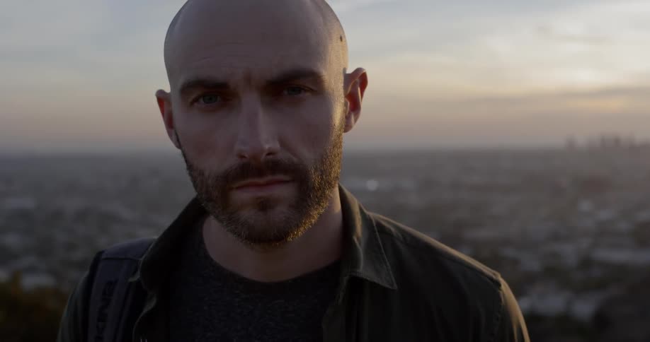A man looks into the camera standing in front of a city
