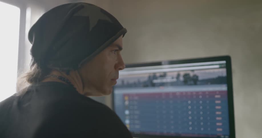 Man wearing black beanie and necklace uses computer in the room during daylight