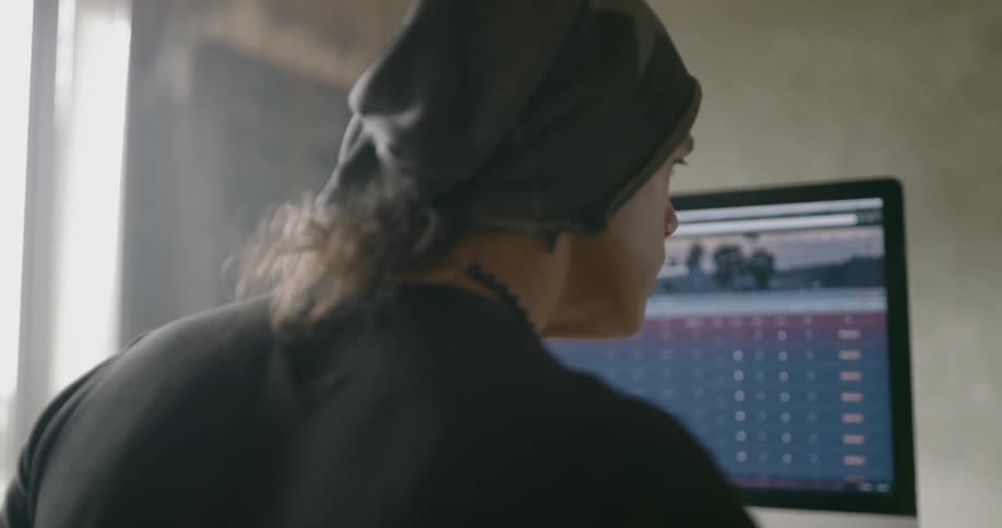 Man wearing black beanie and necklace uses computer indoors during daylight
