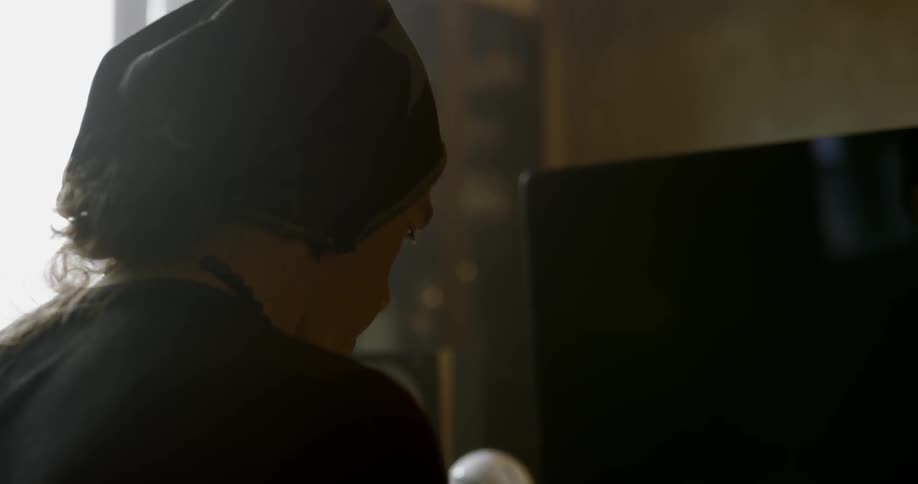 Male wearing a knit cap sitting in front of a screen nodding his head