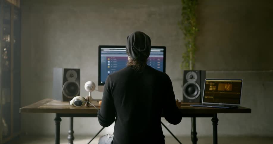 A man works on his computer surrounded by audio equipment and a laptop