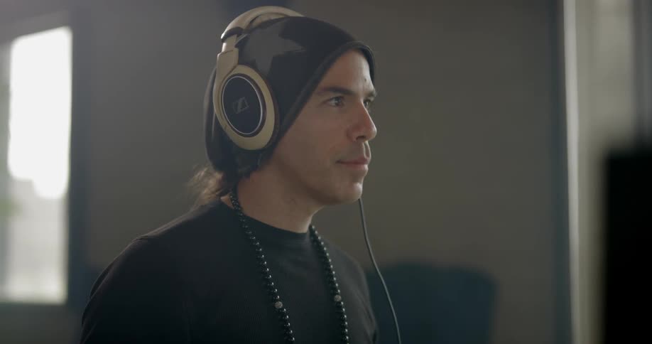 A man wearing a black knitted cap and black beads put on a pair of headphones and starts nodding his head to the beat of the music he is listening to