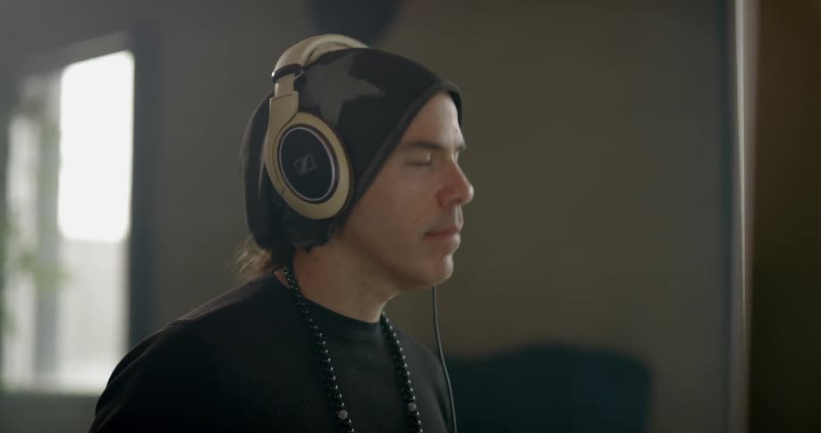 Man wearing headphones listens to music and shakes head indoors during daylight