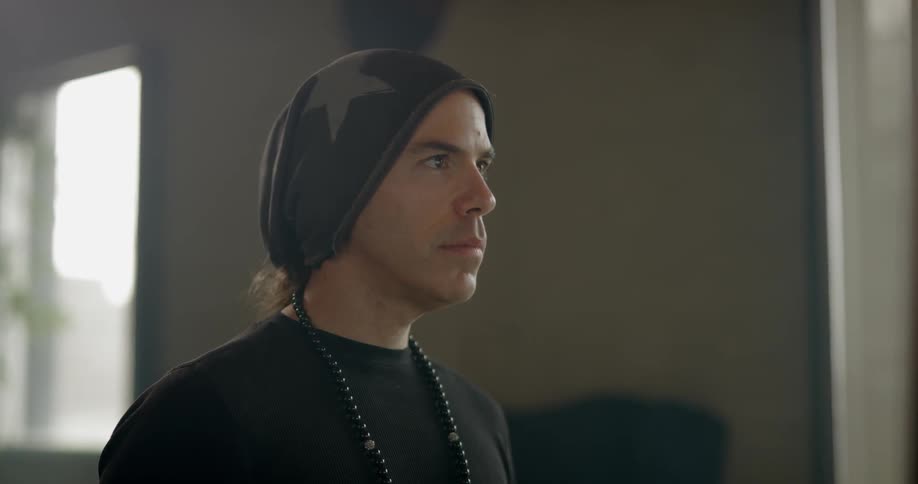 Man wearing beanie and necklace looks at computer display in a room during daylight
