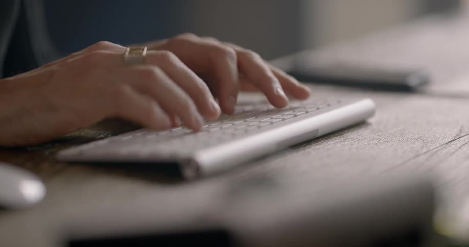 A persons hands as they type on a small wireless keyboard and use a wireless mouse