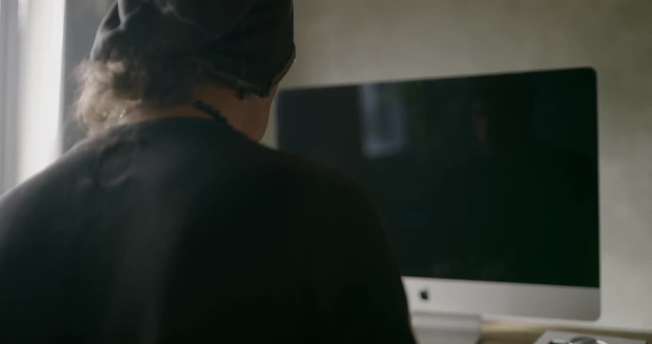 Man wearing black slouchy beaniesits at the table in front of computer display during daylight