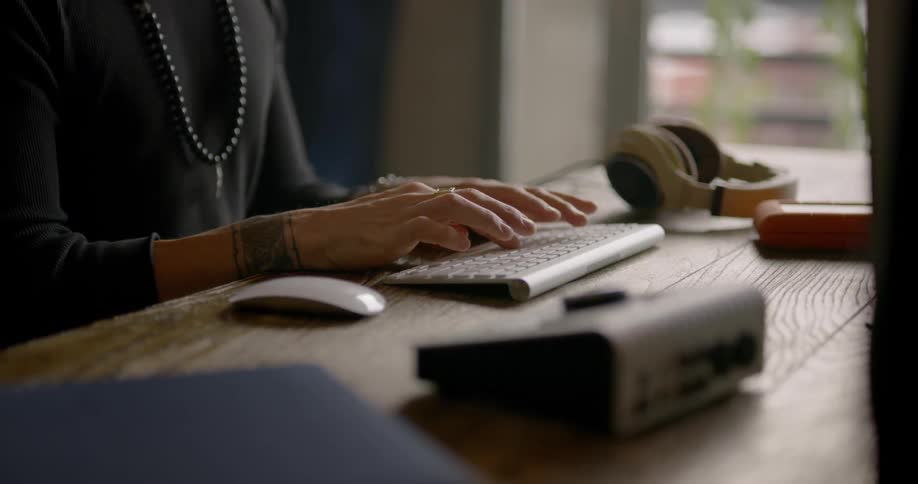 Man wearing black knotted bead necklace sit at the table and types up indoors during daylight