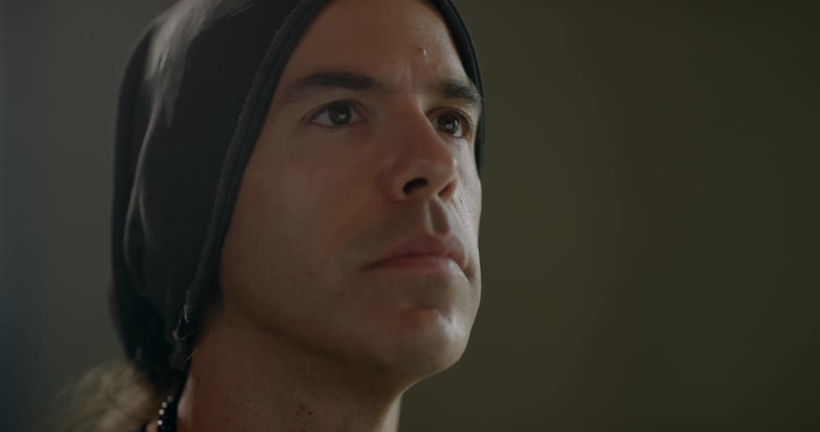 A man wearing a beanie takes off his headphones and bobs his head