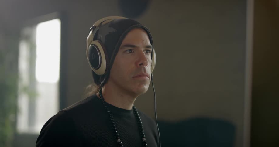 A white man sits at a computer monitor while wearing headphones
