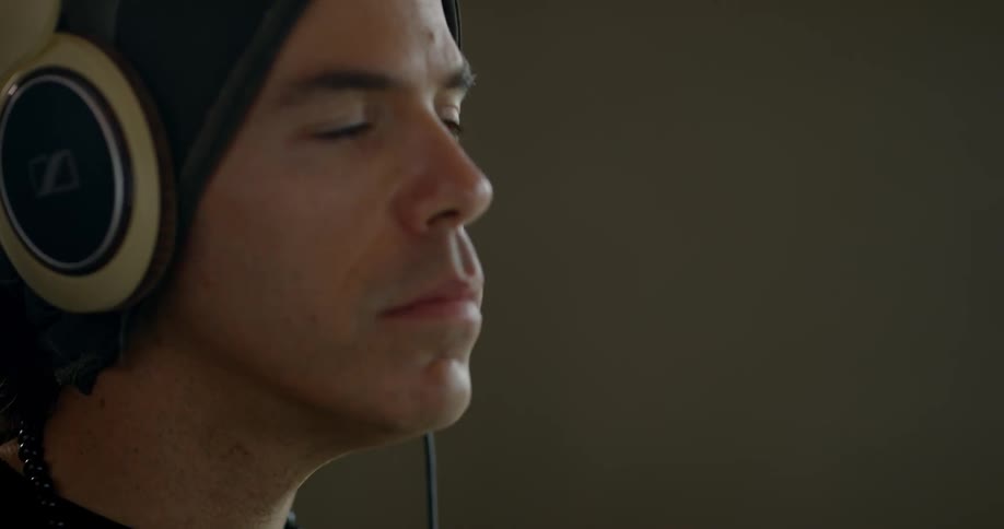 A white man with a beanie puts on headphones and nods his head