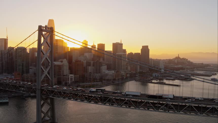 The sun is coming up behind the big cityas the morning traffic crosses the bridge
