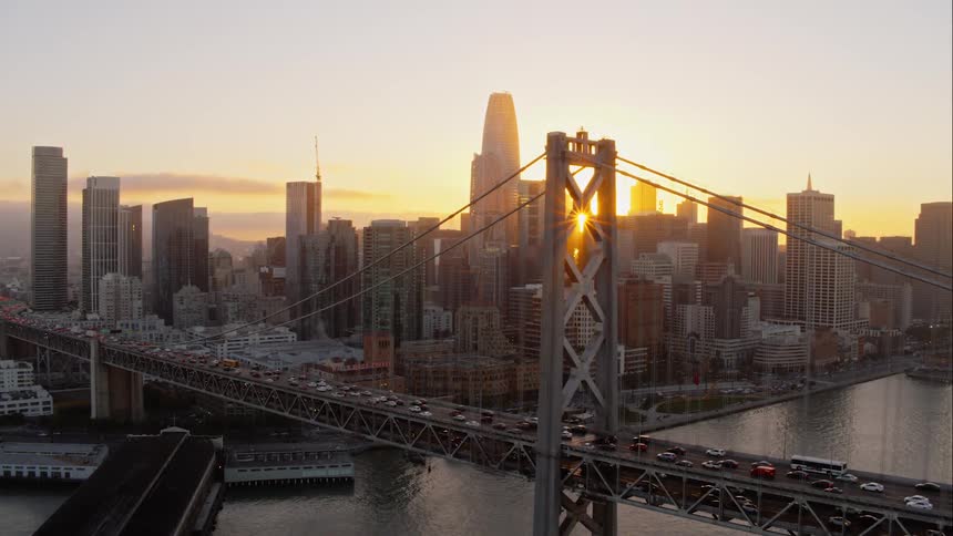 Cars driving across a bridge at sunrise into a city