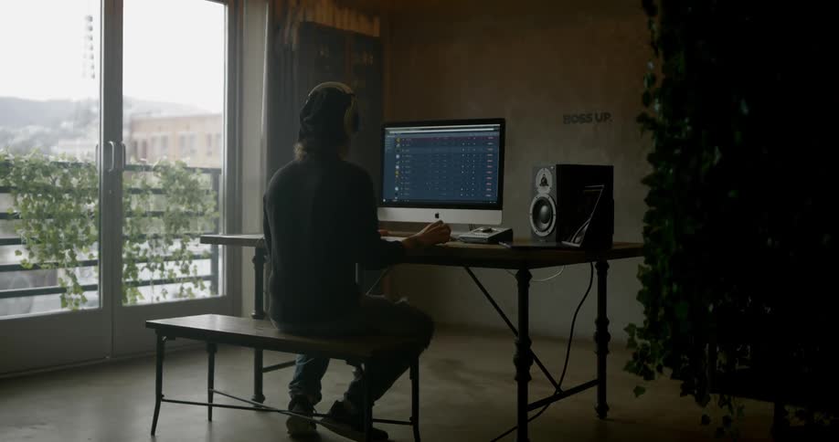 Man sits at computer desk with headphones on
