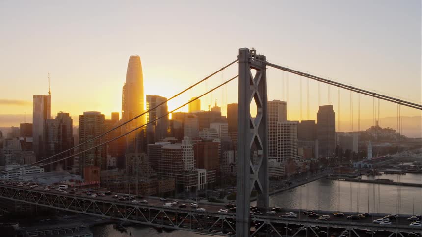 Cars drive across a bridge in to and out of a city at sunset