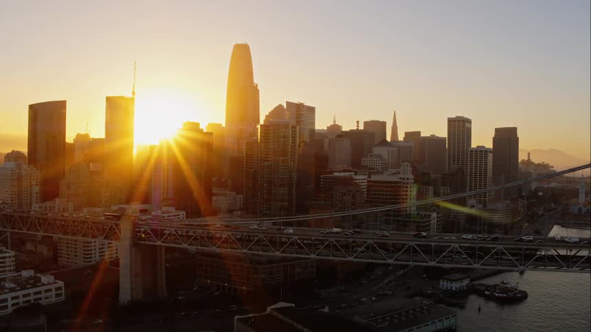 A suspension bridge over a river in a large city during sunset