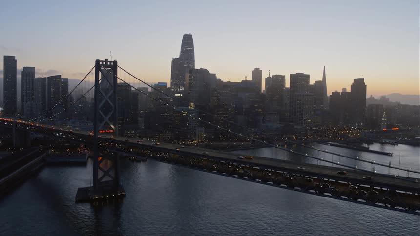 Cars travel across a bridge with a city skyline at sunset