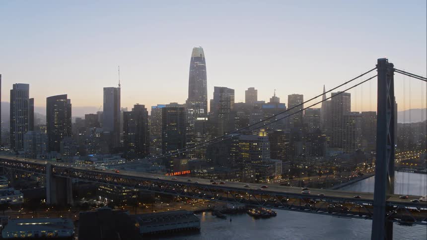A suspension bridge over a river near a large city skyline