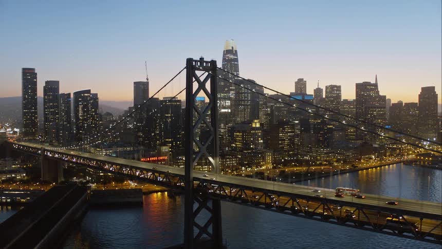 Skyline of the illuminated city while the cars go over the bridge at dusk