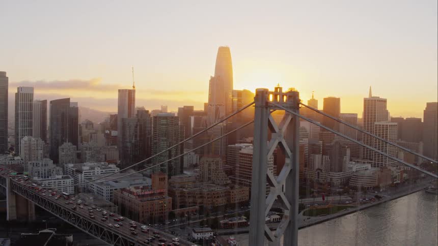 Skyline of the city with tall buildings and cars going over the bridge while the sun goes down behind the buildings