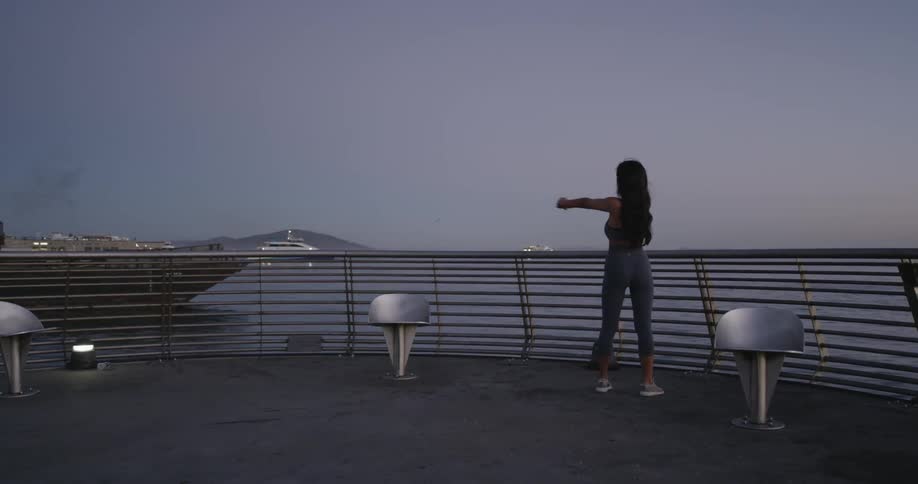 Woman stretches her arms on the promenade next to the dock at dawn