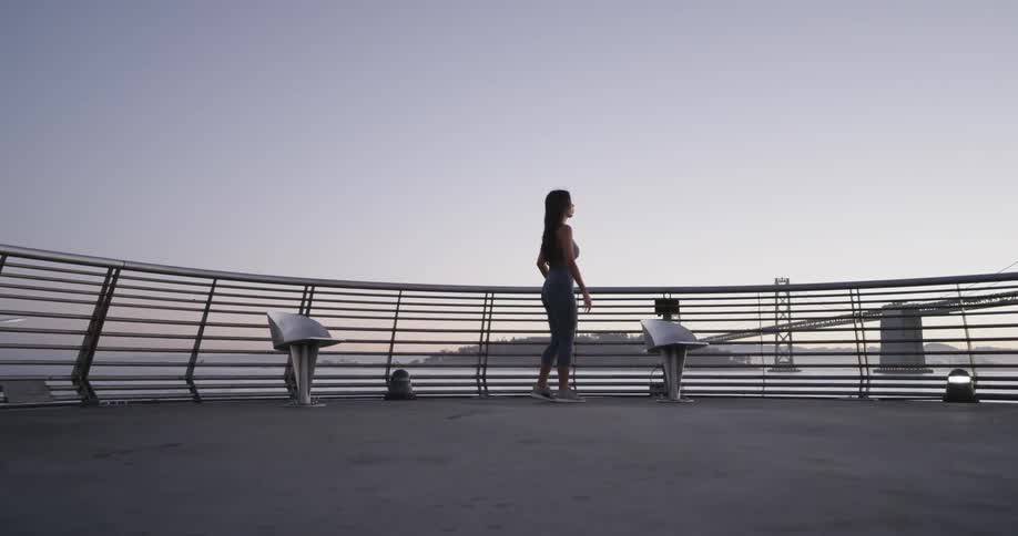 A female jogger doing stretches on a platform overlooking a body of water