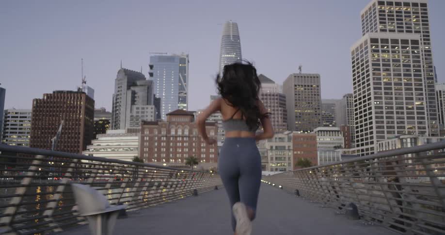 A woman runs across a pedestrian bridge toward a large city