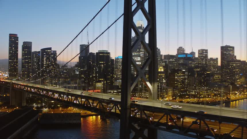 Cars drive on a city bridge in front of skyscrapers at dusk