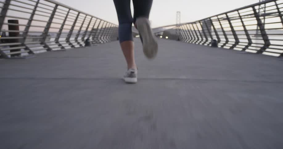 A woman in leggingsjogs along a pier at low sun