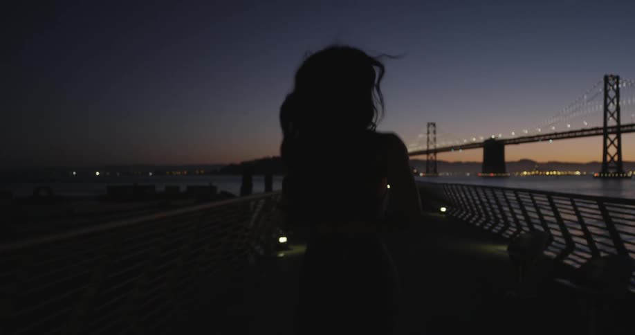 A woman jogs along a city walkway at sunset