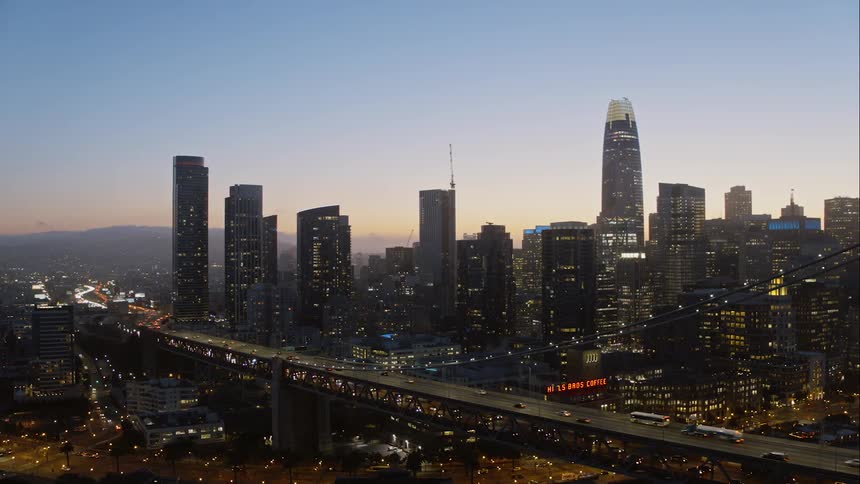 Cars drive along a bridge next to a city skyline at sunset