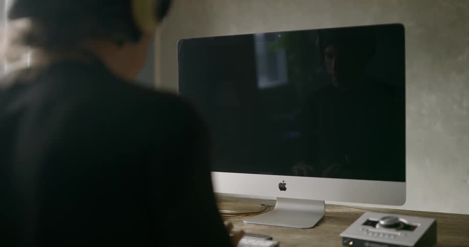 Man sitting at the table in front of apple computer display types on keyboard and shakes his head in a room during daylight