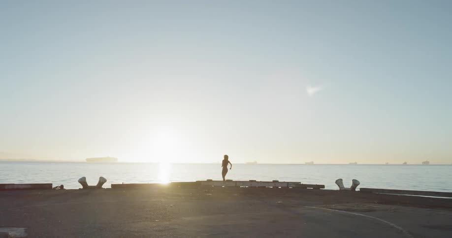 A woman jogs along a pier near the ocean at sunrise