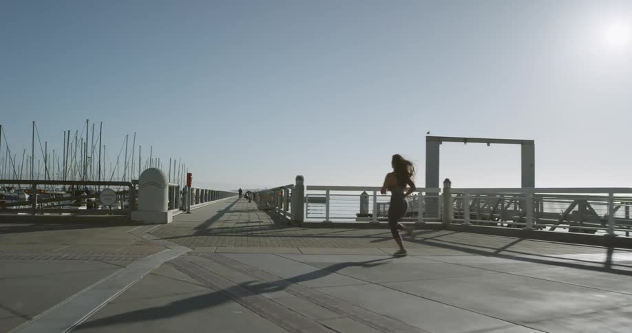 A woman runs down a pier in a shipyard