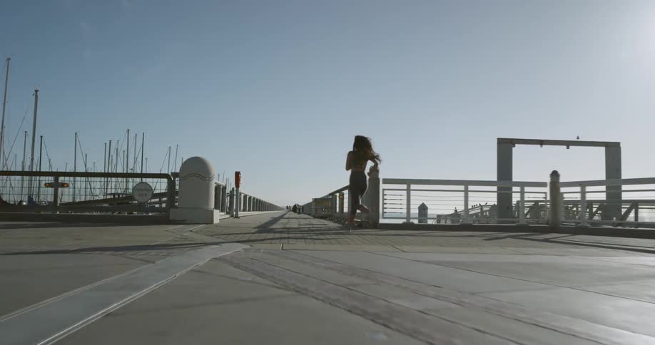 Woman jogs along bridge bordering marina and ocean