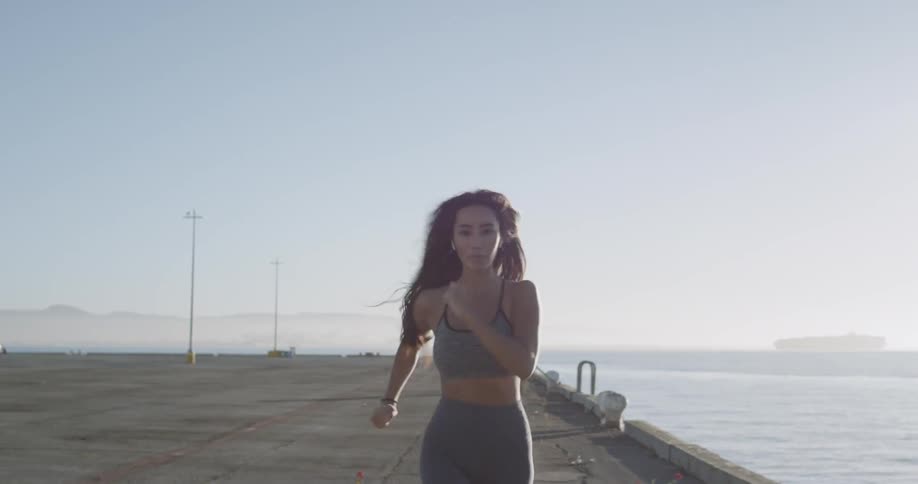 A woman is jogging along on a cement pier near the water