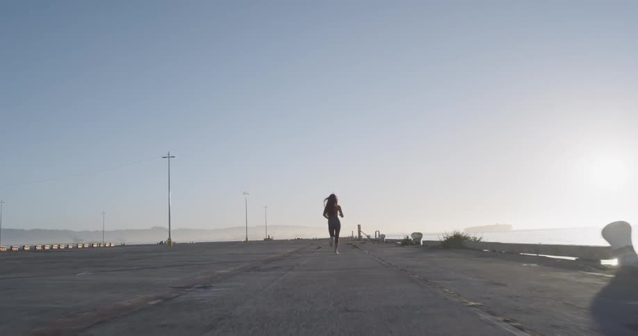 A female jogging down a concrete pier during the day