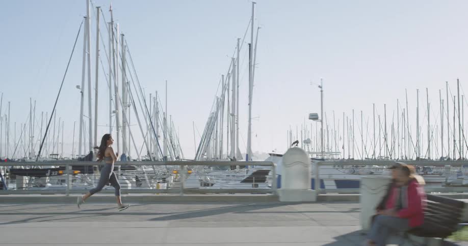 A woman runs along a pathway beside a boat marina